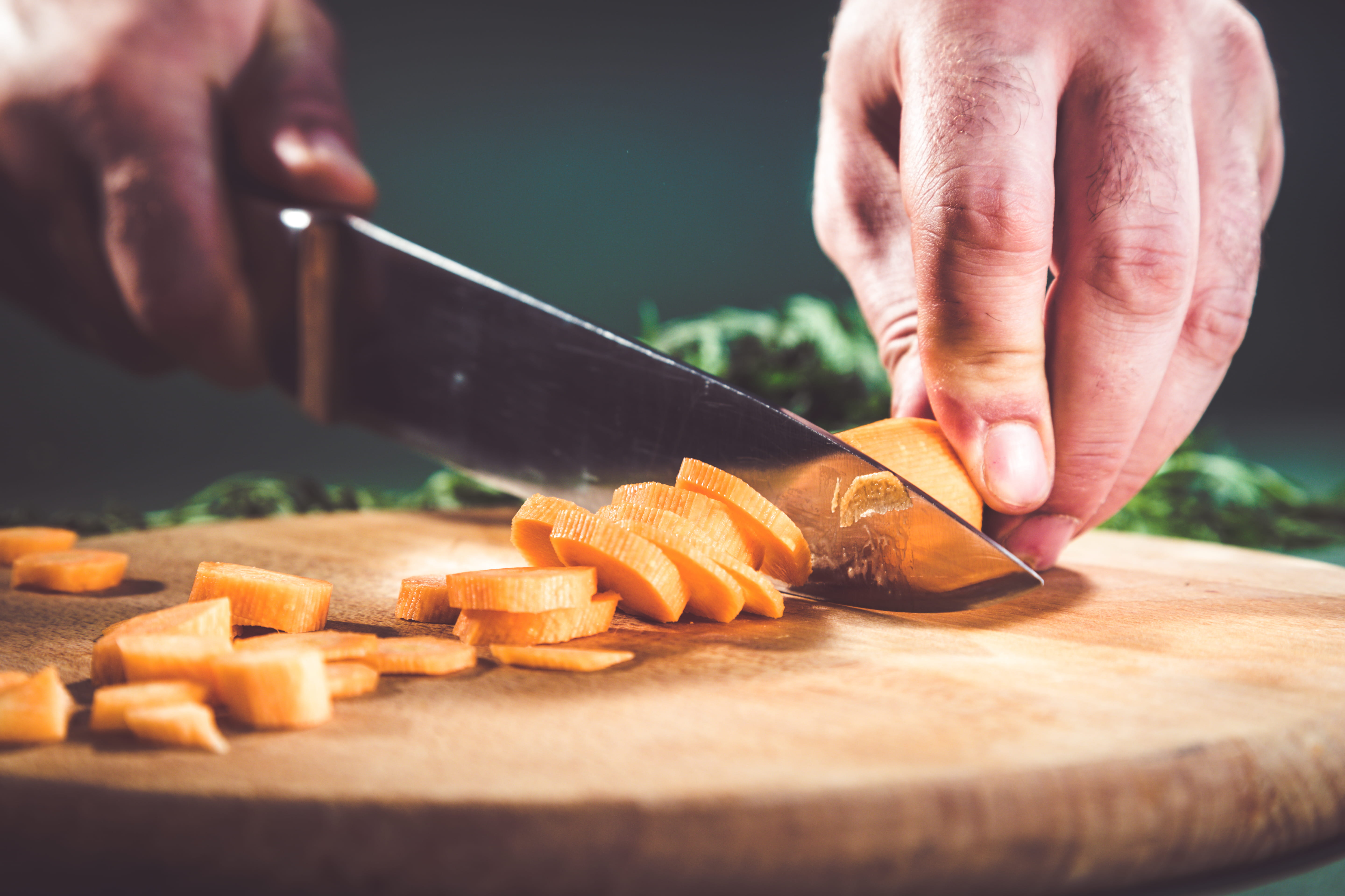 Close up of professional chef cutting carrot on a chopping board 